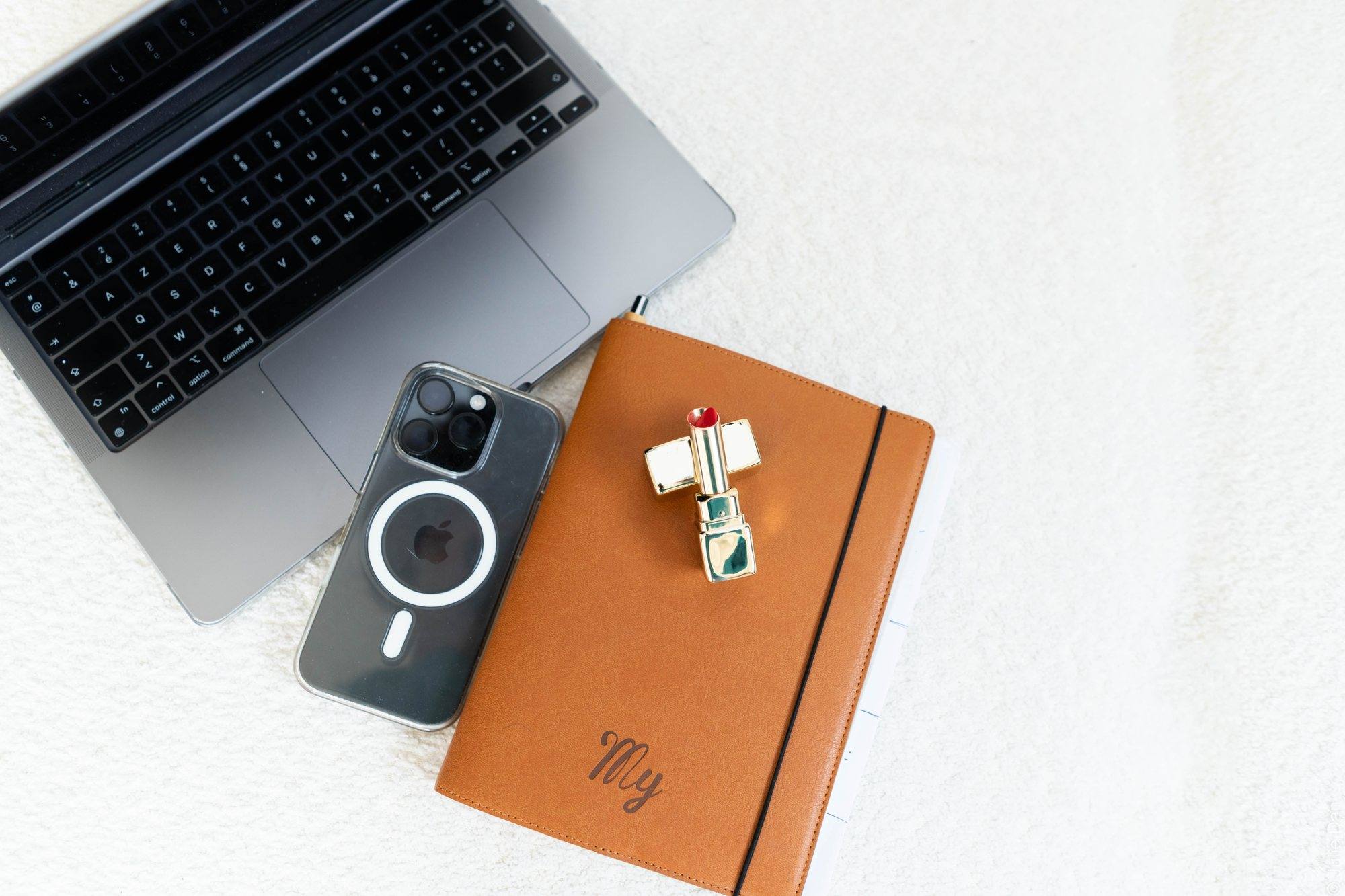 Ordinateur portable, téléphone et carnet en cuir posés sur un bureau blanc