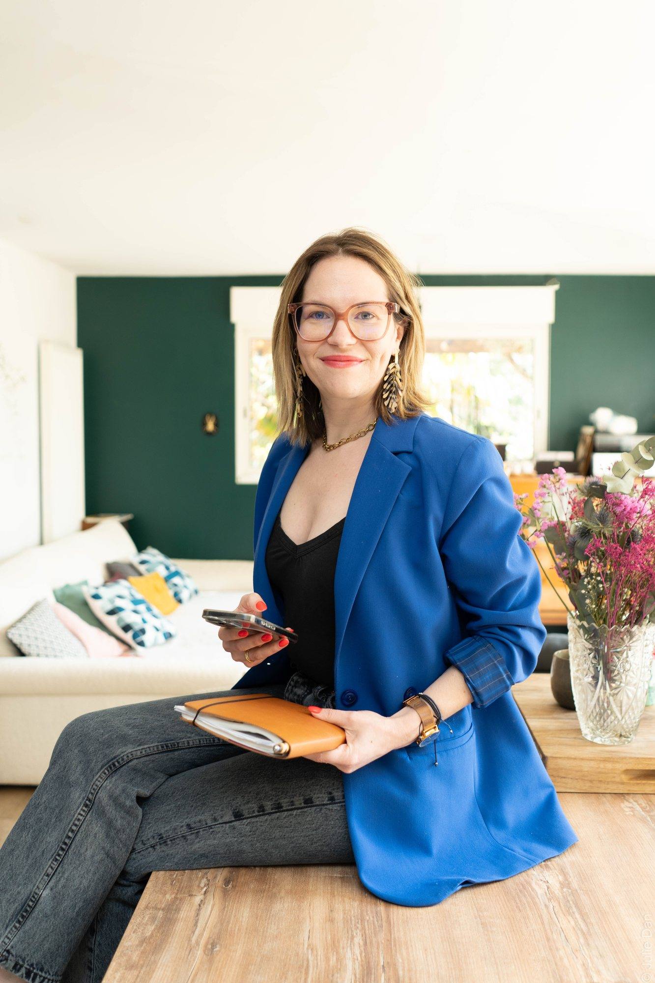 Virginie Pinsault tenant son agenda, assise dans un salon lumineux au mur vert