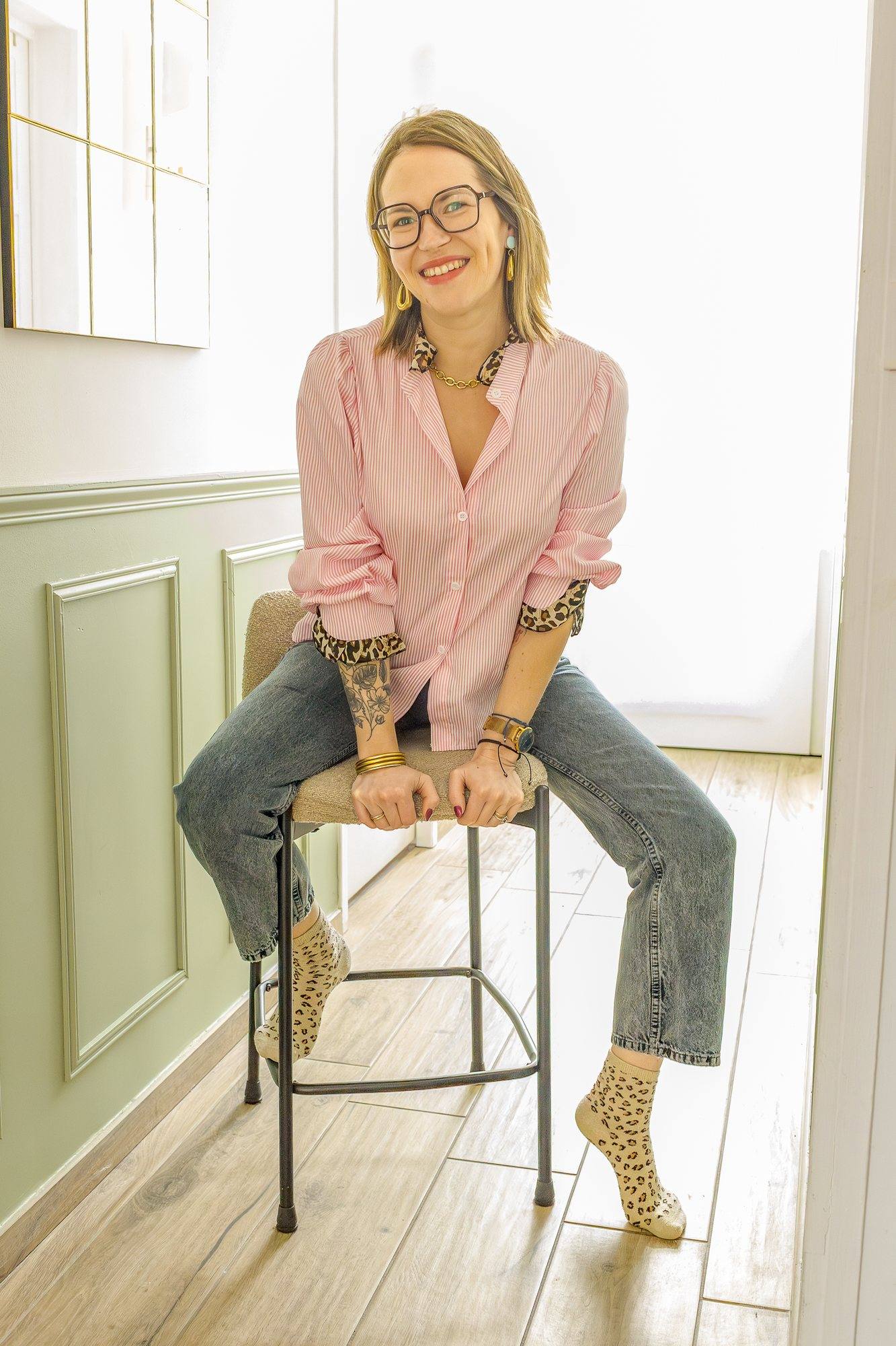 Virginie Pinsault, home organiser, souriante sur un tabouret dans une entrée aux boiseries vert sauge